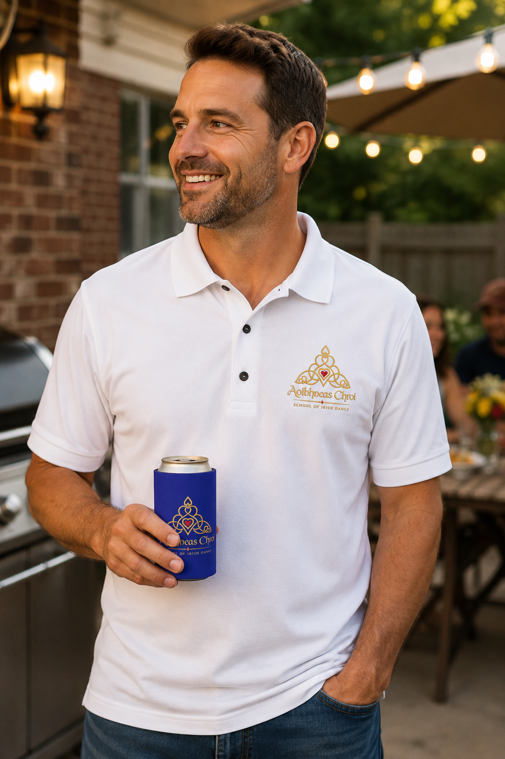 A man wearing a white polo shirt with a custom printed logo on the left chest, holding a blue can cooler with a matching logo, set in an outdoor backyard environment.