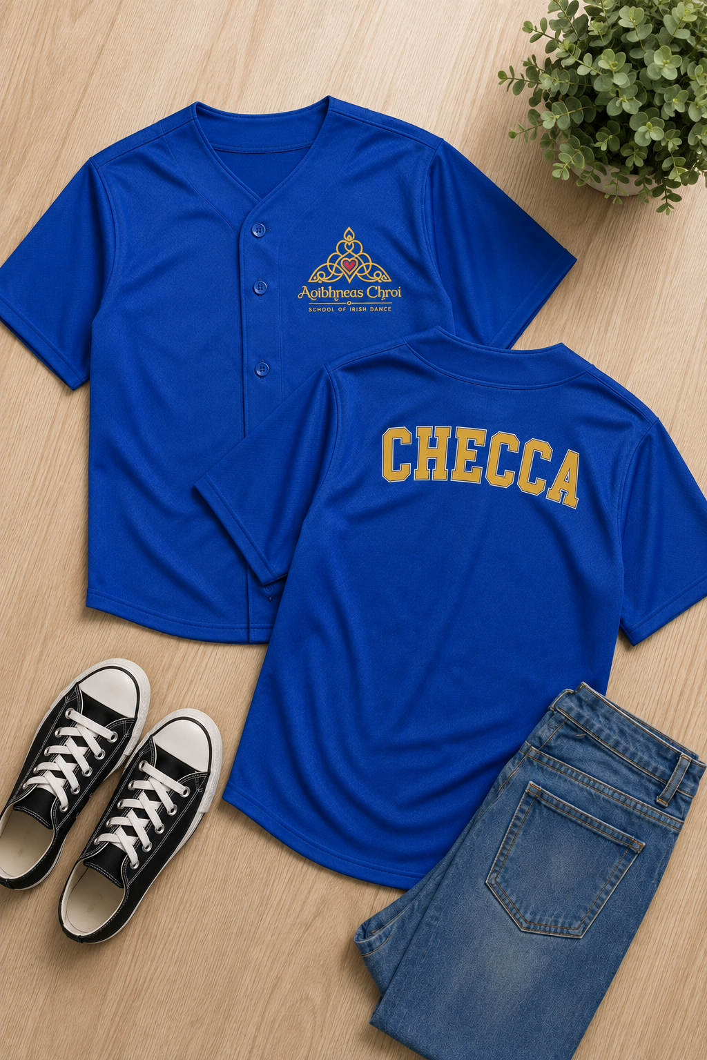 Two royal blue athletic t-shirts displayed in a flat lay on a light wood floor, styled with black sneakers and blue jeans. The front shirt features a small gold and white 'Anthropos Christ' emblem, and the back shirt features 'CHECCA' printed in gold arched lettering.