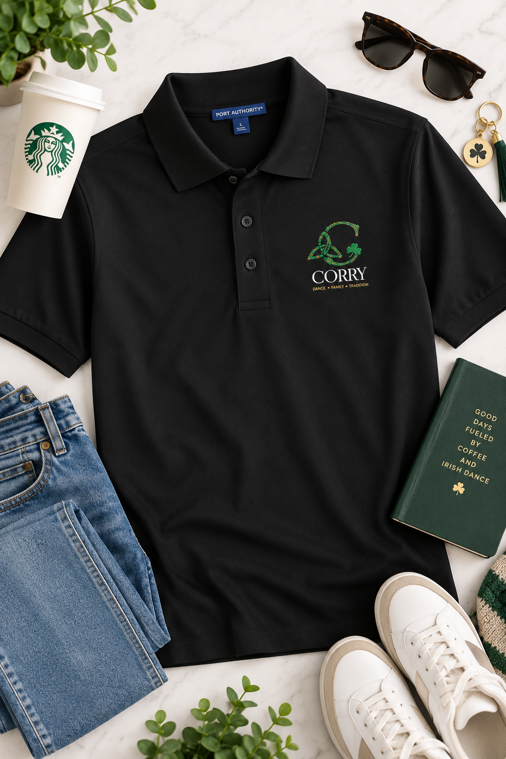 A black short-sleeve polo shirt laid flat on a light marble surface, styled with jeans, white sneakers, sunglasses, a Starbucks cup, keys, and a green book. The shirt has a green and gold 'Corry' graphic on the left chest.