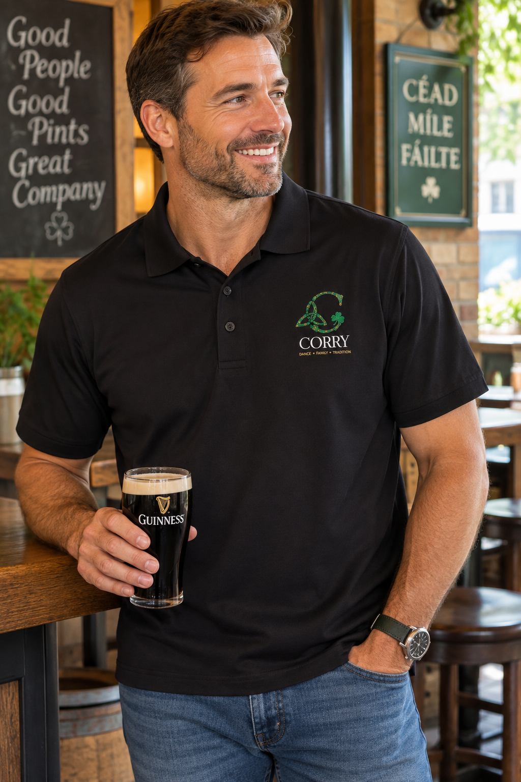 A man in a pub wearing a black polo shirt with a green and white 'Corry' logo on the chest, holding a pint of Guinness. The background features wooden bar stools, brick walls, and Irish-themed signs.
