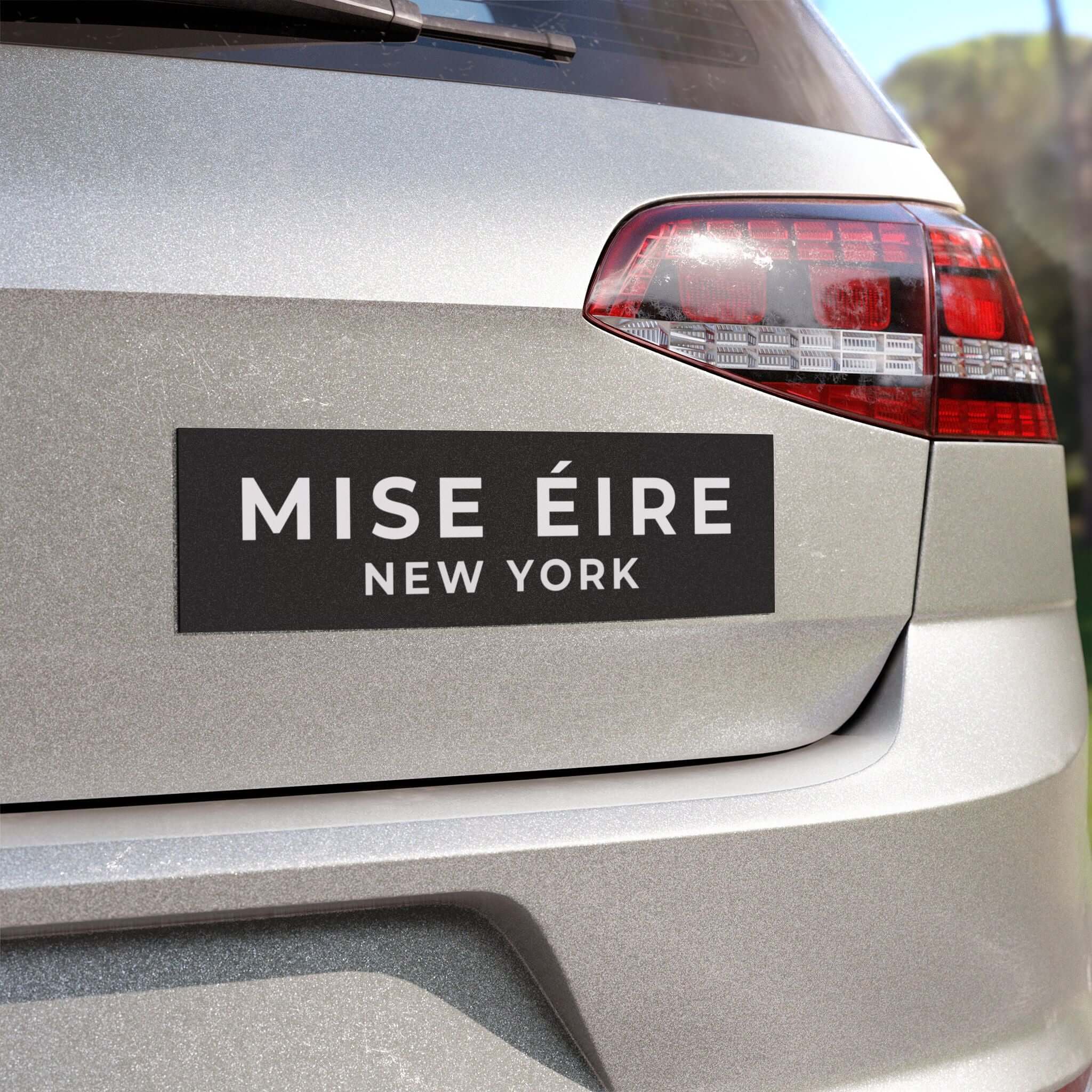 A rectangular black car sticker with white text reading 'MISE ÉIRE NEW YORK' applied to the rear trunk of a silver vehicle.