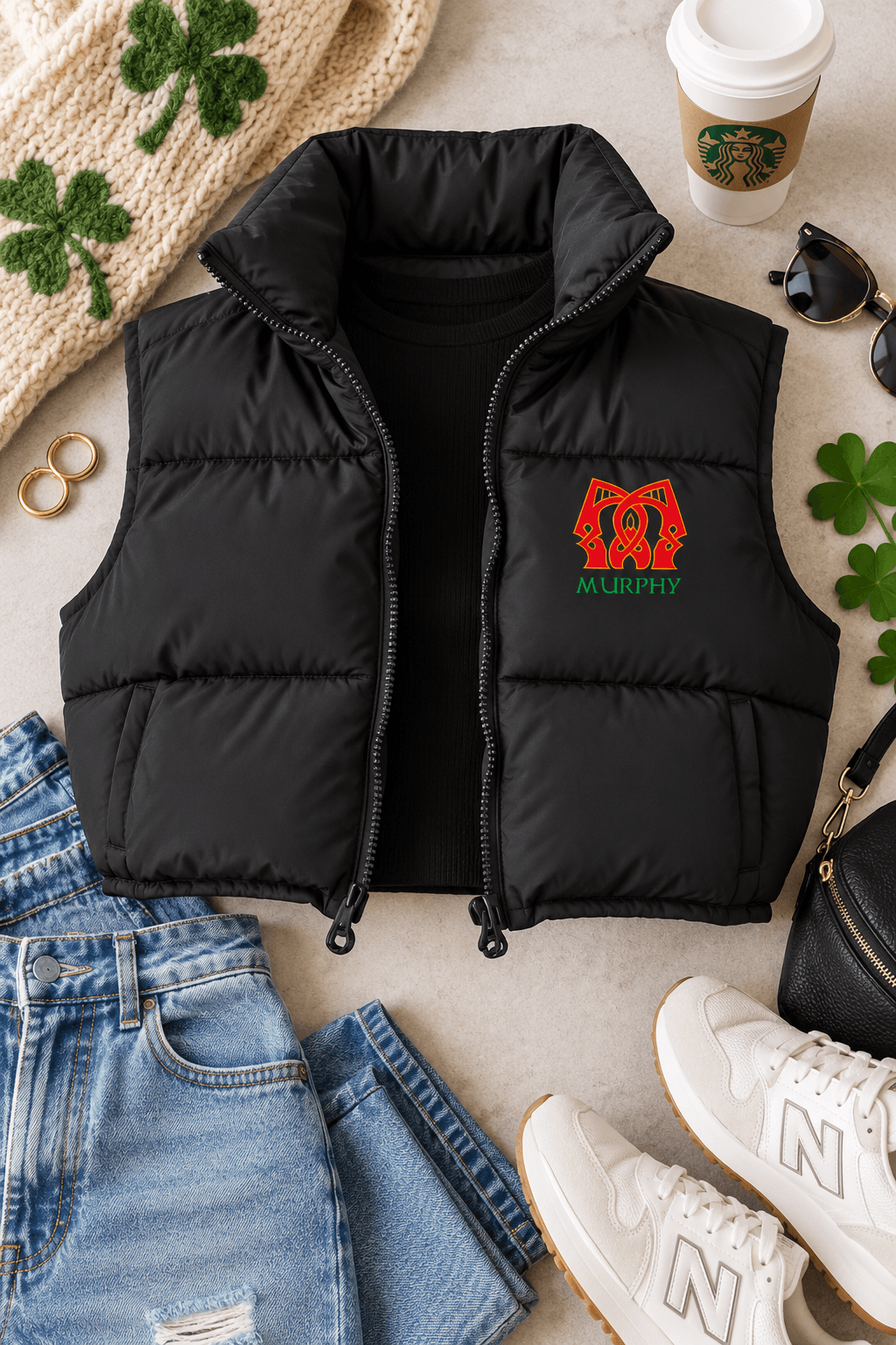 A black puffer vest laid flat on a light beige surface, styled with jeans, white sneakers, sunglasses, a Starbucks cup, a knit hat, and shamrock accents. The vest has a red and green embroidered design on the left chest featuring a horse head and the word 'Murphy'.
