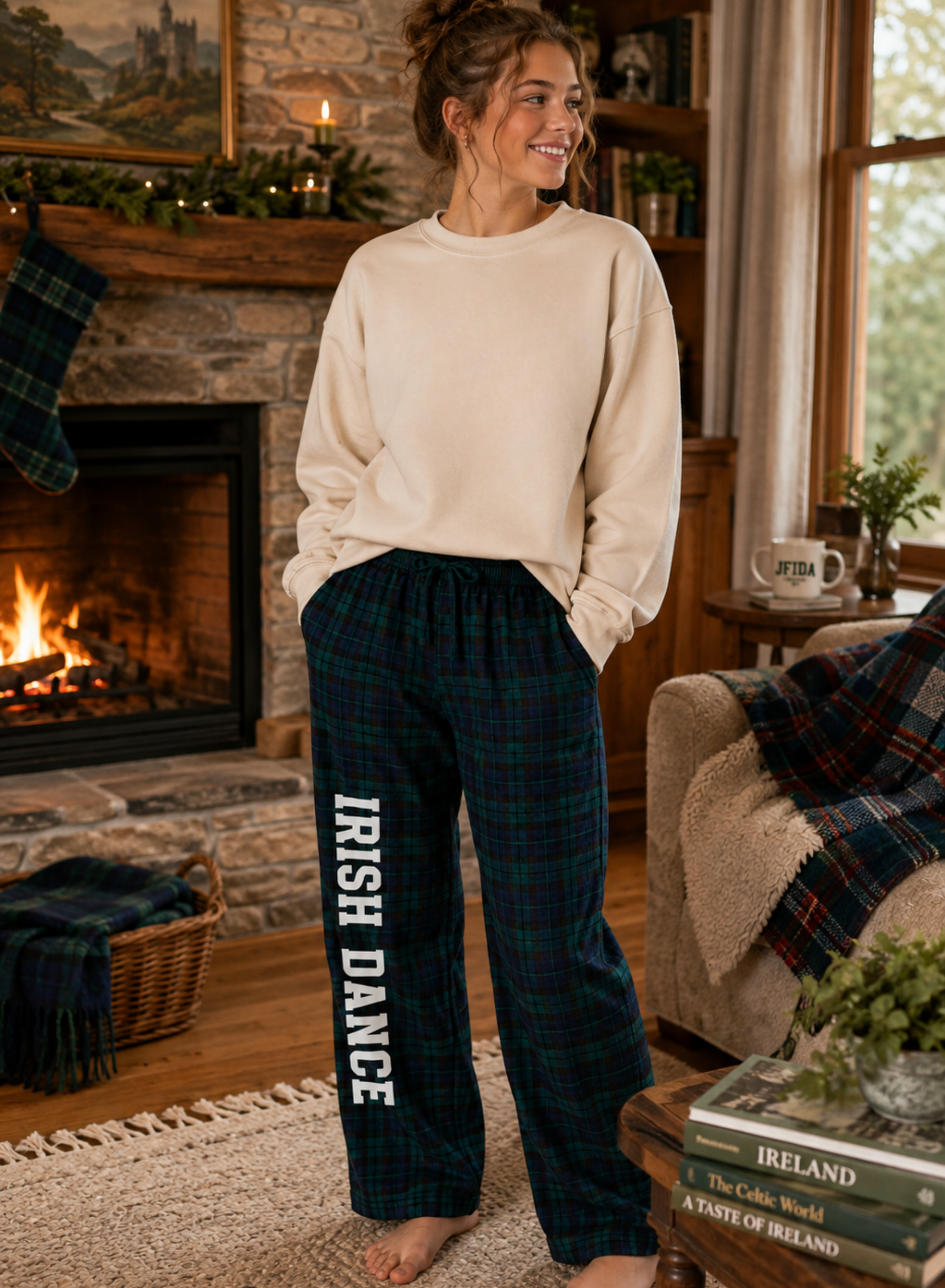 A woman stands barefoot in a cozy living room wearing cream sweatpants and dark green plaid sweatshirt pants with 'IRISH DANCE' printed vertically in white. The room features a fireplace, a fireplace mantel, and a couch with a plaid throw blanket.