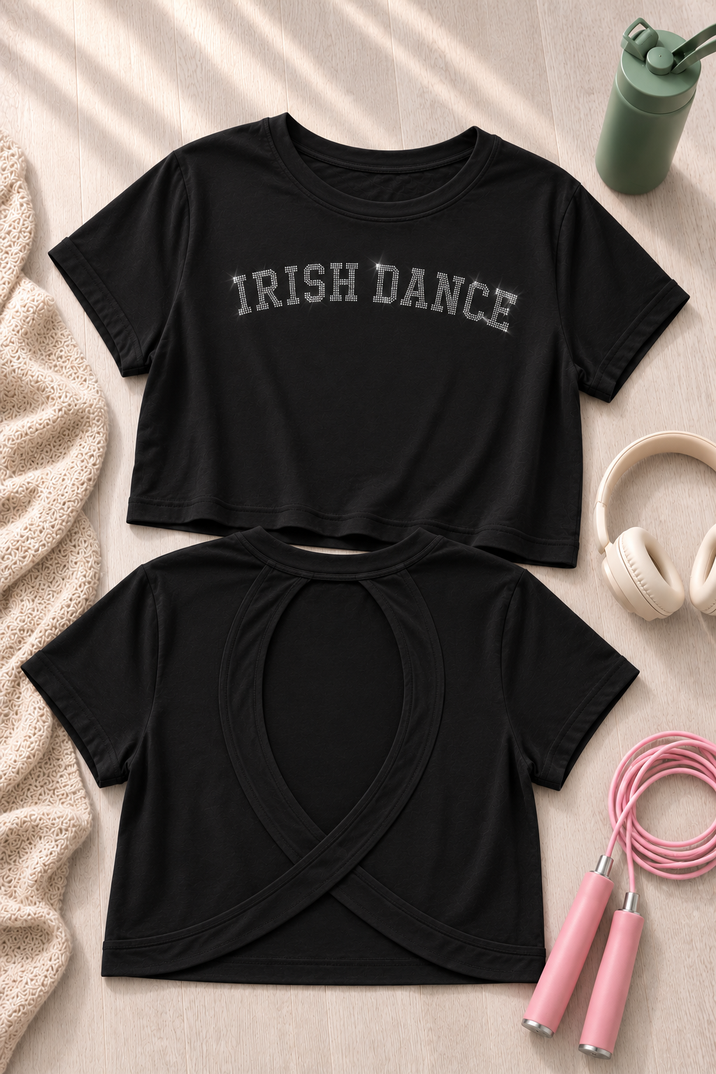 Two black short-sleeve crop top t-shirts laid flat on a light wood surface. The top shirt has 'IRISH DANCE' printed across the chest in gray.