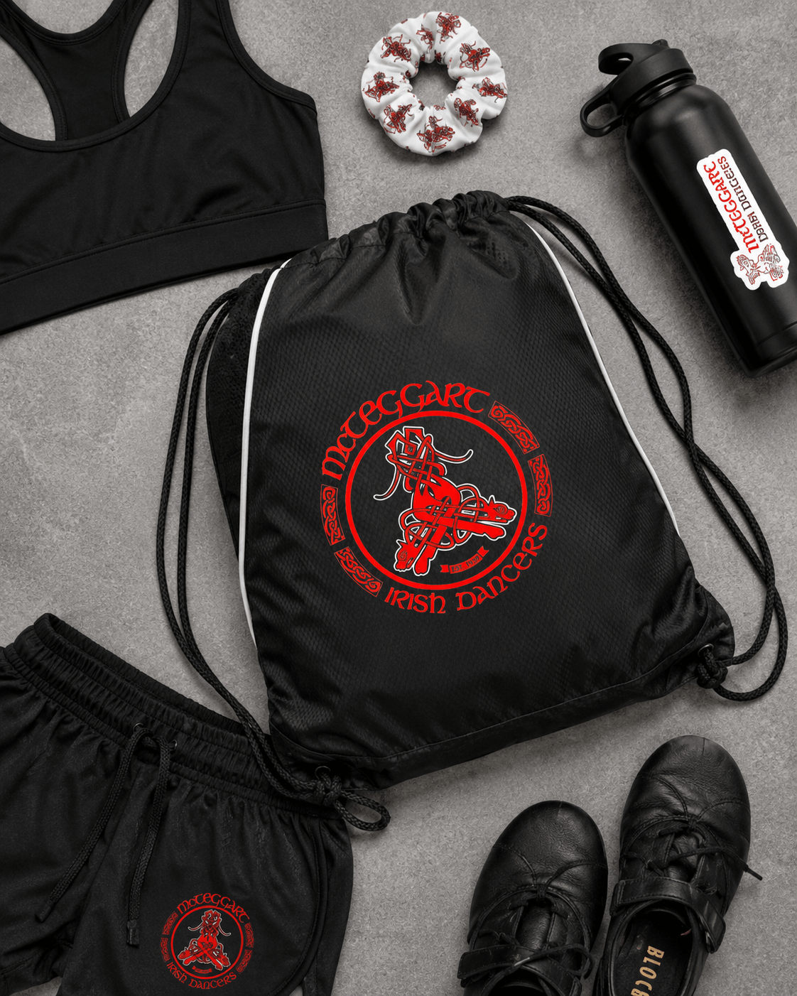 mcteggart irish dancers, A flat-lay arrangement of black athletic gear with a red and white 'McTeggart' graphic, including a drawstring bag, shorts, a sports bra, a water bottle, a scrunchie, and shoes on a gray textured background.