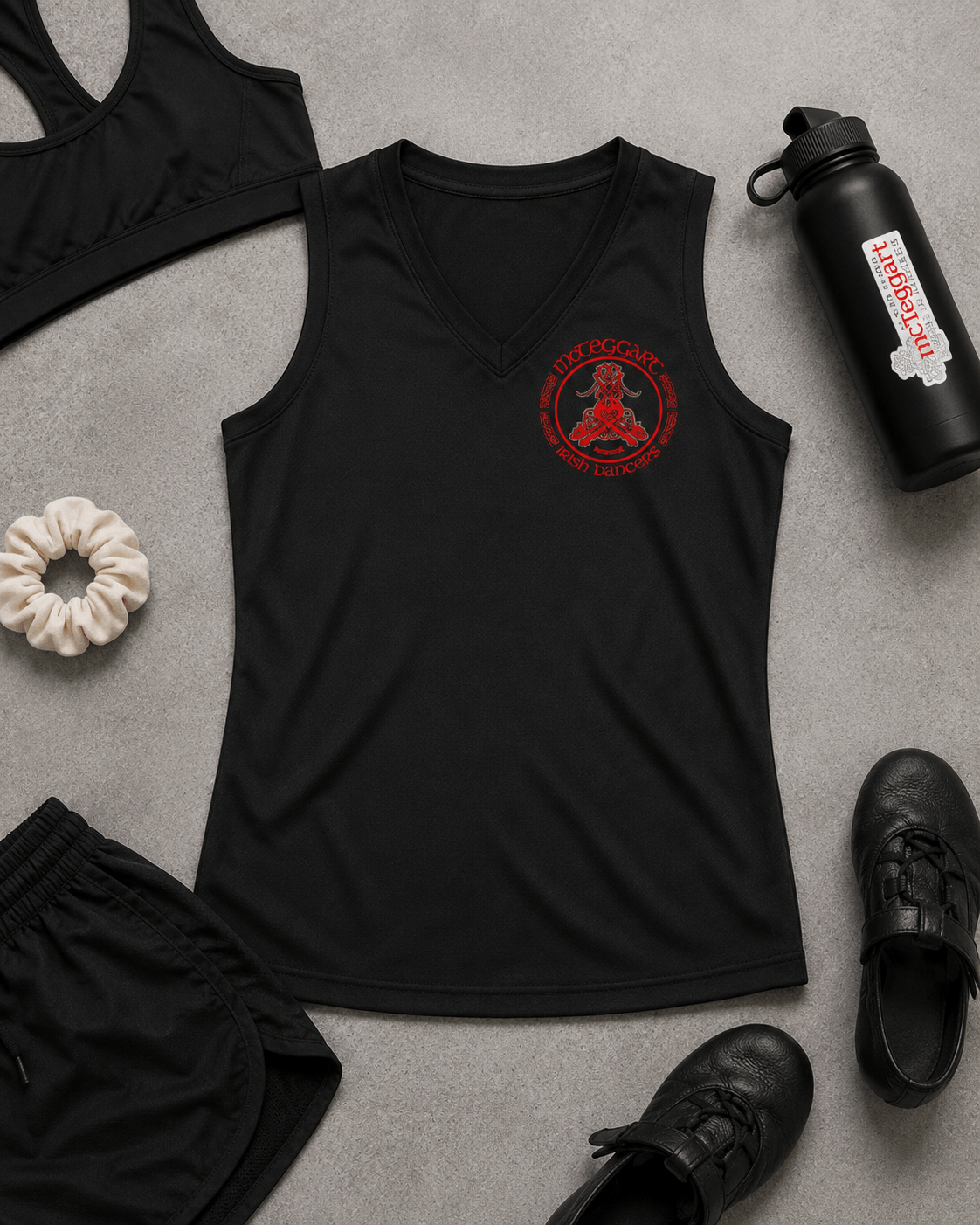 mcteggart irish dancers, A black sleeveless athletic tank top laid flat on a gray surface, featuring a red circular chest graphic with a seated figure and the words 'McTeggart' and  Surrounding props include black shorts, a black sports bra, a black water