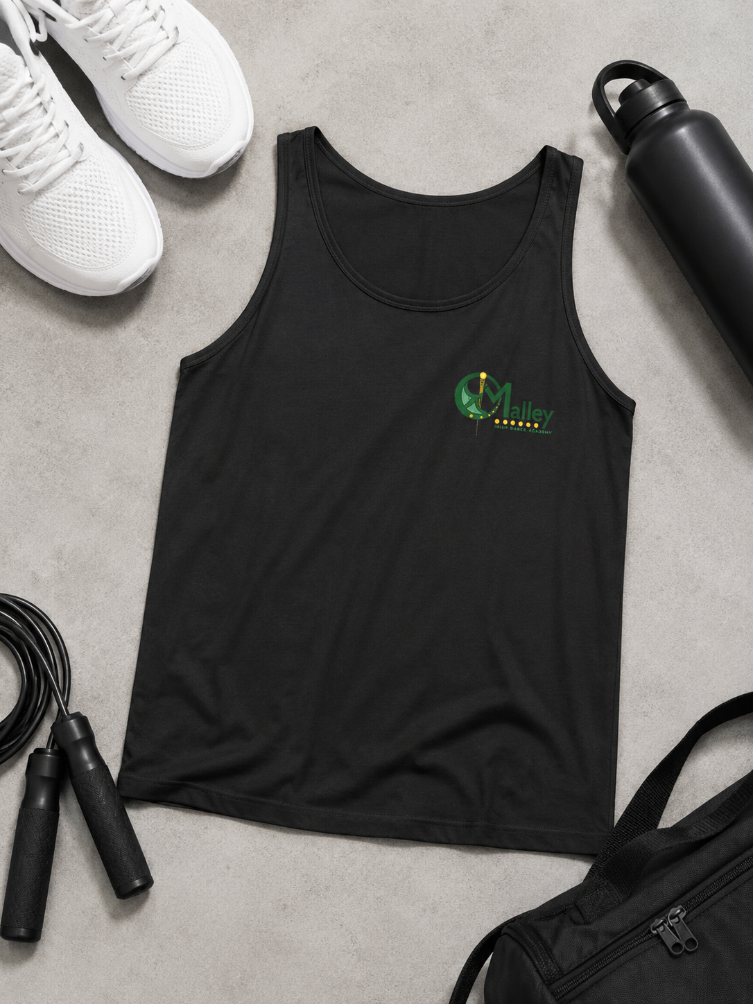 A black sleeveless tank top laid flat on a light gray surface, featuring a small green and yellow chest graphic. Surrounding props include white sneakers, a black water bottle, a jump rope, and a black bag.