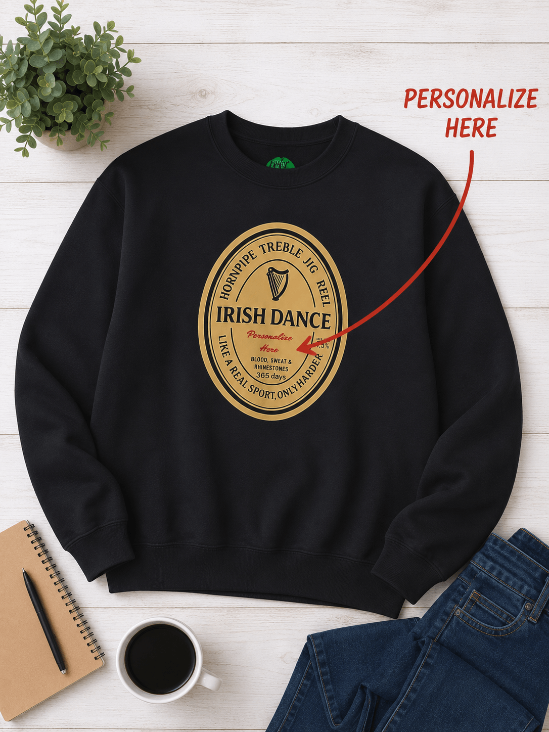 A black crewneck sweatshirt laid flat on a white wood background, featuring a circular gold graphic that reads 'Irish Dance' with a harp and guiness style print
