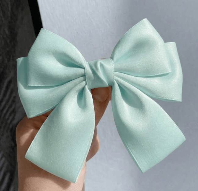 A large mint green satin bow held by a hand against a light gray background.