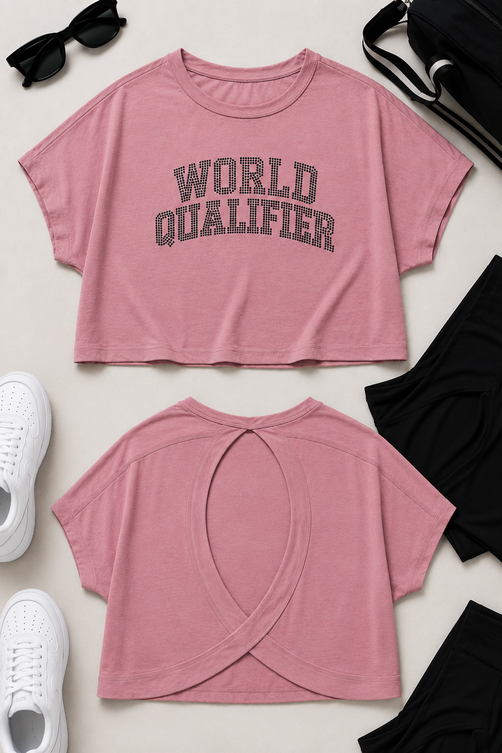 A pink short-sleeve crop top shown from both front and back in a styled flat lay. The front has dark gray varsity-style lettering that reads 'WORLD QUALIFIER.